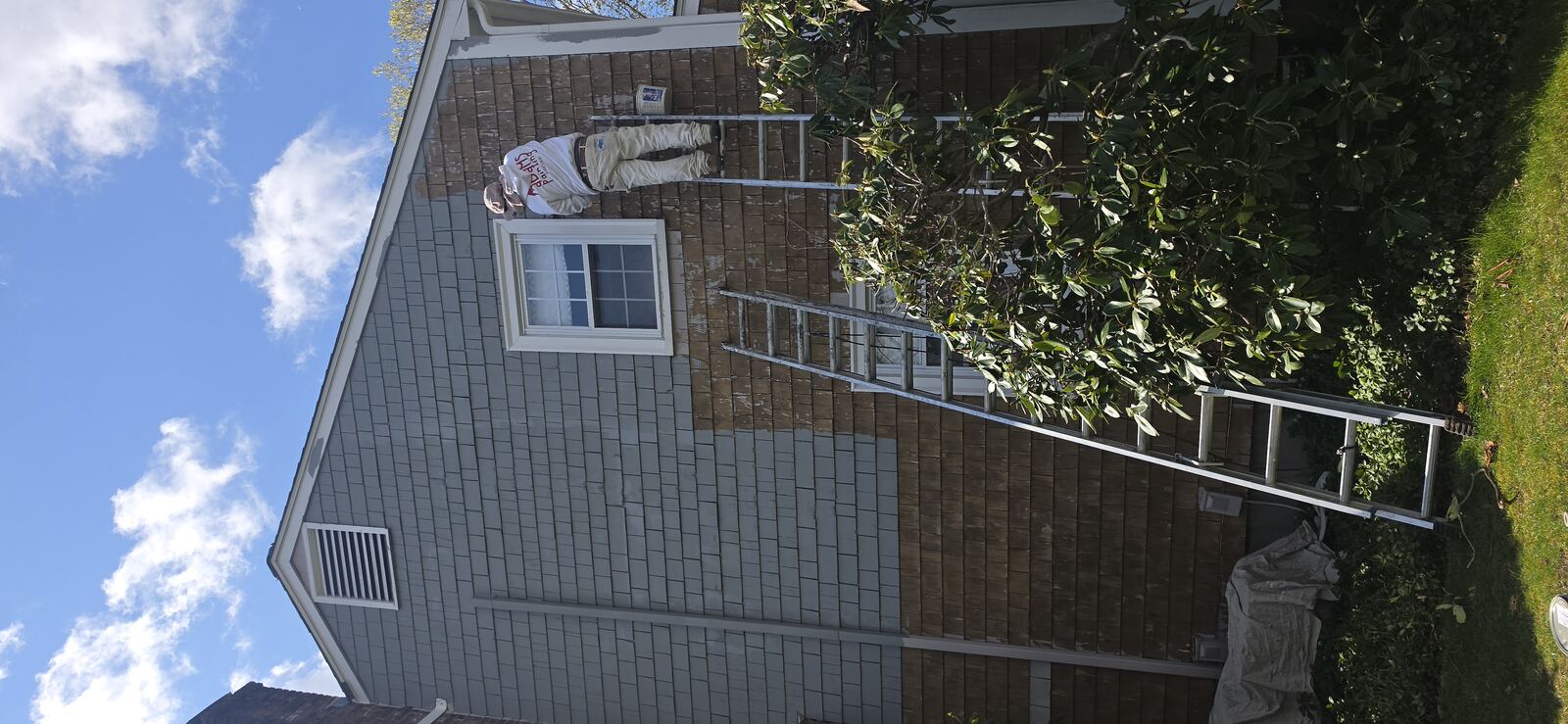 Painter on tall ladder repainting cedar shake siding grey